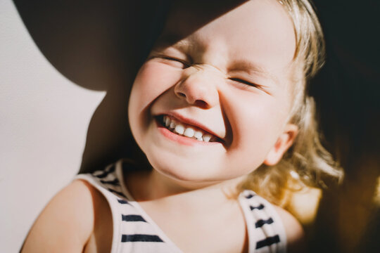 Cutest little girl smiling and squinting in sunlight. Happy toddler having fun. Portrait of playful child preschool age. Lifestyle photography.