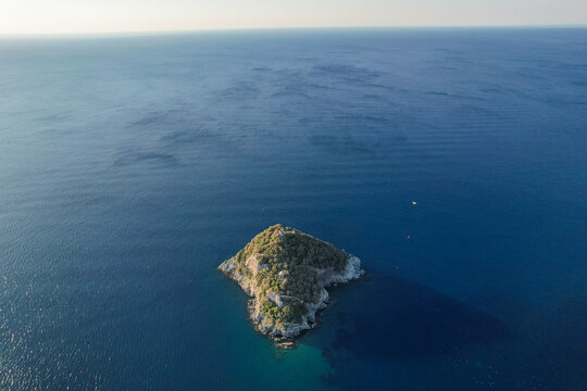 Aerial view of Tino Island, its rugged terrain contrasting with the deep blue sea, a solitary haven of green amidst the vast expanse of the Ligurian coast, Liguria, Italy.