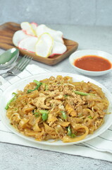 Char Kway Teow, fried flat rice noodles with egg, and vegetables on a white plate, Indonesian dish.