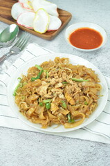 Char Kway Teow, fried flat rice noodles with egg, and vegetables on a white plate, Indonesian dish.