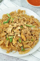 Char Kway Teow, fried flat rice noodles with egg, and vegetables on a white plate, Indonesian dish.