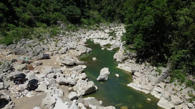 White rocks dominate the scene at Tinipak River, Tanay Rizal, with black-roofed nipa huts nearby and the river flowing gently&mdash;captured in a smooth forward aerial shot.