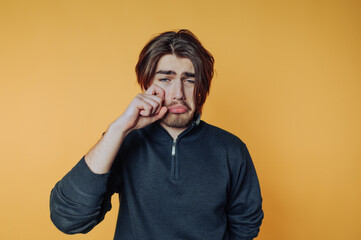 portrait of young man displays sorrow with a sad expression and tears on yellow background
