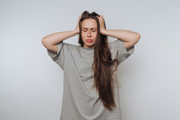 Fototapeta premium portrait of young frustrated woman holds her head in both hands, depicting clear signs of stress on light background