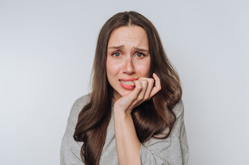 portrait of young woman bites her nail, showcasing anxiety and worry on light background
