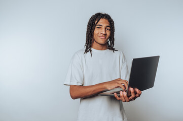 portrait of young man stands with a laptop, smiling cheerfully, showcasing remote work culture on light background