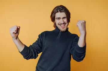 portrait of young man is celebrating with raised fists and a big smile, exuding happiness and...