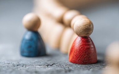 Two small wooden figurines, one blue, one red, stand at the edge of a line of similar figures