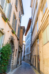 Fototapeta premium Paving stones empty narrow Italian street in Como city. Multicolor old house building architecture. Medieval village summer mood.