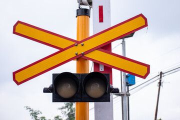 Close up view of a railway level crossing, marked by a prominent yellow and red X sign and a traffic light system.