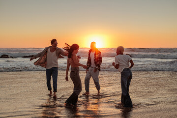 Friends dancing together on the beach at sunset