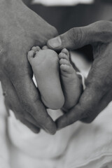  Black and white close-up of a parents hands forming a heart around a newborns tiny feet. Emotional and timeless image for concepts of love, family, parenthood, and tenderness 