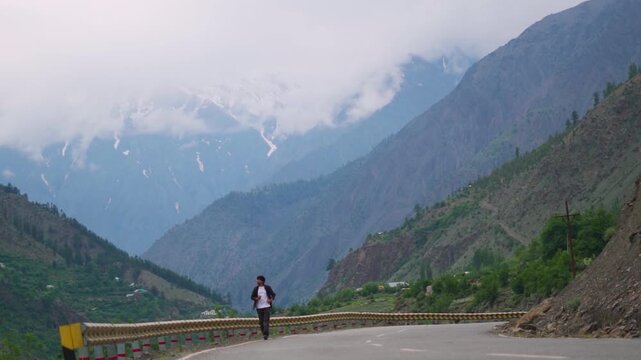 Defocused Indian man running towards the camera in front of Himalayan mountain ranges covered by clouds during the monsoon season near Udaipur in Pattan Valley, Lahaul, Himachal Pradesh, India. 