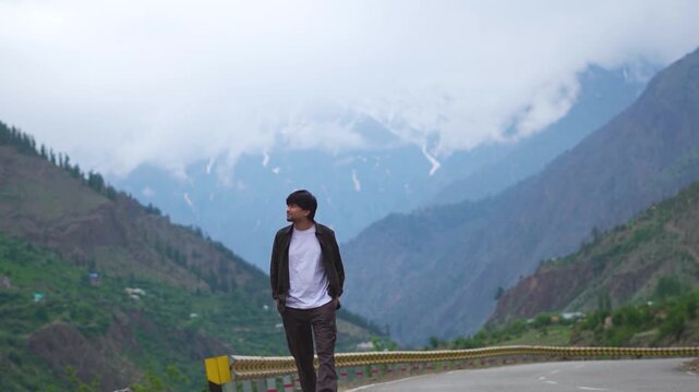 Portrait shot of an Indian man walking in front of snowy Himalayan mountain peak covered by clouds during the monsoon season near Triloknath village in Pattan Valley, Lahaul and Spiti, Himachal, India
