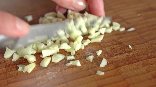 Close-up. Female hands chopping garlic finely on a wooden board.