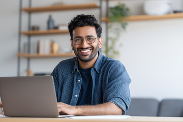 Naklejka premium Happy Indian man in glasses with laptop working at home for remote job concept