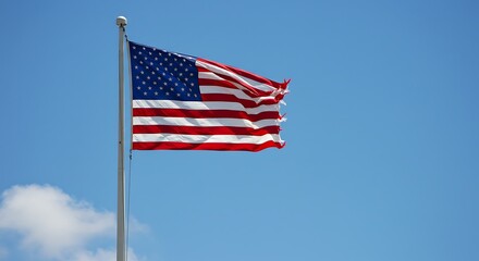 Obraz premium Tattered american flag waving in the wind against a clear blue sky background