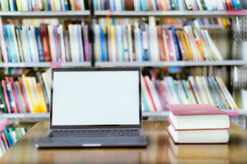 There is a laptop with a white screen and a book placed on the table in the library.
