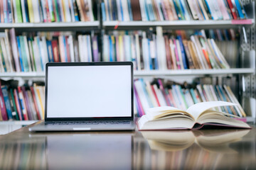There is a laptop with a white screen and a book placed on the table in the library.
