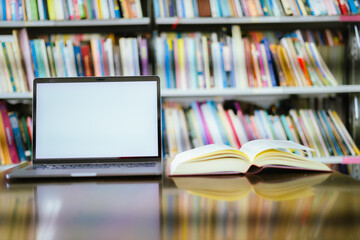 There is a laptop with a white screen and a book placed on the table in the library.
