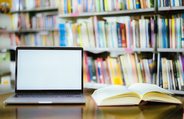 There is a laptop with a white screen and a book placed on the table in the library.
