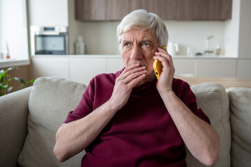 Suspicious stressed elderly man frowns during unexpected call, listening to pressured demands for banking information. Fraud warning, social engineering pressure, personal data risk, financial scam