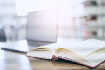 There is a laptop with a white screen and a book placed on the table in the library.
