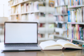 There is a laptop with a white screen and a book placed on the table in the library.
