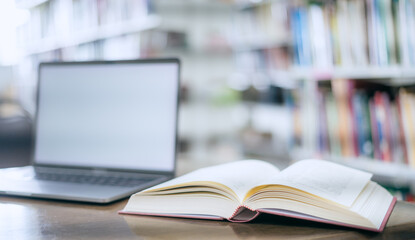 There is a laptop with a white screen and a book placed on the table in the library.
