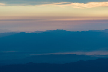 Sunset over misty layered mountains, evoking hope, reflection, and timeless beauty. Golden sunset casting warm light over layers of mountain ridges, with soft mist and pastel-colored sky 