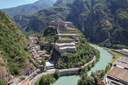 Aerial view of the imposing Fort Bard perched atop a rocky hill, overlooking the Dora Baltea river and nestled among verdant mountains, Bard, Aosta Valley, Italy.