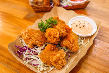 Close-up of crispy Japanese karaage chicken served on shredded cabbage with sesame mayo dipping sauce on wooden table.

