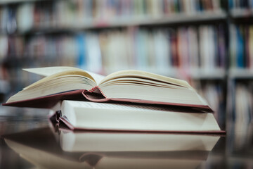 Open book with books piled up on the table in the library. Basic education concept.