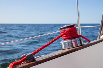 Sailboat winch with red rope of genoa headsail sheet in jammer on yacht deck. Detailed close-up with shallow depth of field, highlighting sailing equipment, marine life, and nautical craftsmanship