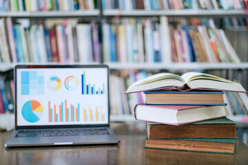 A laptop screen displaying a graph and a book placed on the table in the library, representing a business concept.

