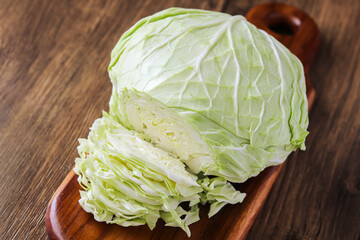 Fototapeta premium A fresh head of green cabbage, partially sliced into thin shreds, resting on a wooden cutting board. The image highlights the crisp texture of the vegetable.