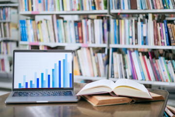 A laptop screen displaying a graph and a book placed on the table in the library, representing a business concept.
