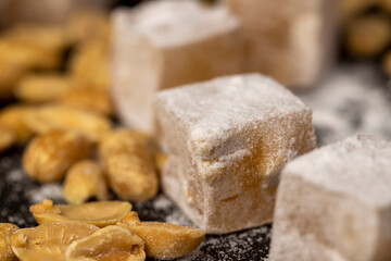 Turkish delight scattered on the table, sugar cubes with starch and toasted peanuts on a black slate surface, closeup, side view