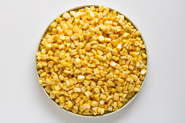 Top-down view of a round bowl or plate overflowing with bright yellow corn kernels, set against a clean white background.