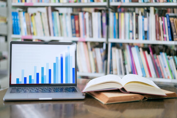 A laptop screen displaying a graph and a book placed on the table in the library, representing a business concept.
