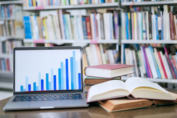 A laptop screen displaying a graph and a book placed on the table in the library, representing a business concept.
