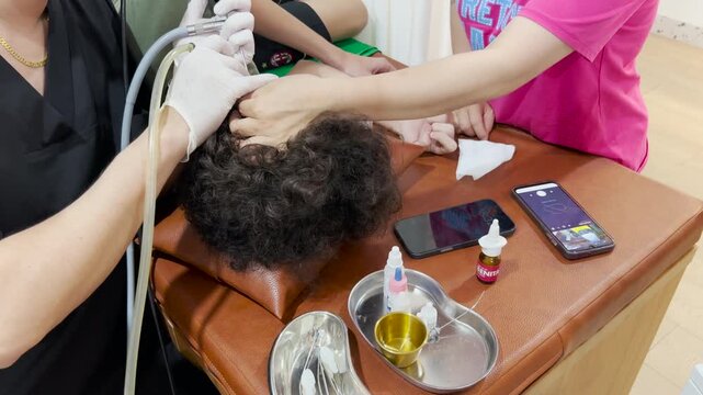 The patient lies on the examination chair while the doctor cleans the ear using special tools. The procedure is monitored on a screen.