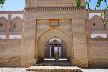 Fototapeta premium Woman standing at the Entrance of Amir Tura Madrasah and Walled Fortress known as Itchan Kala in Khiva, Uzbekistan - ウズベキスタン ヒヴァ イチャン カラ アミール トゥラ メドレセに立つ観光客の女性