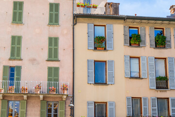 Windows with green wooden shutters. Flowers in pot on balcony. Italy summer day. Italian style facade. Wall house architecture background.