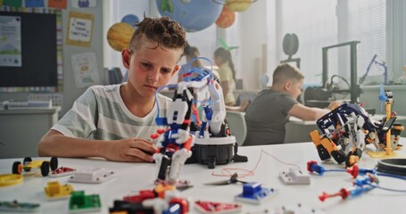 Fototapeta premium Talented Young Boy Studying Robotic Arm Model. Primary School Student Learning Science and Robotics Technology in Modern Classroom, Dreaming to Become Engineer. Creative Activity, STEM Education.