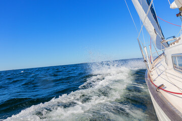 Fototapeta premium Luxury sailing yacht under genoa and mainsail cutting through waves of the Baltic Sea, Gulf of Finland. View from deck to bow, mast, and sails, emphasizing speed, motion, and yachting adventure