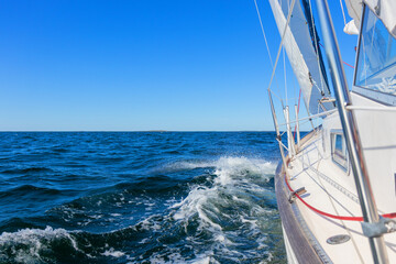 Obraz premium Luxury sailing yacht under genoa and mainsail cutting through waves of the Baltic Sea, Gulf of Finland. View from deck to bow, mast, and sails, emphasizing speed, motion, and yachting adventure