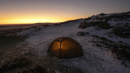 A wild camping tent on a snowy hill in England at dawn