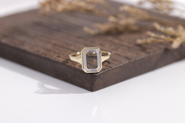 Elegant gold ring with an emerald-cut clear gemstone, displayed on a wooden surface for a minimal...