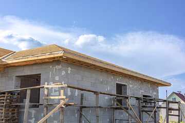Obraz premium A residential house under construction with exterior walls made of light gray concrete blocks, wooden roofing and scaffolding. Housing development in a residential area.